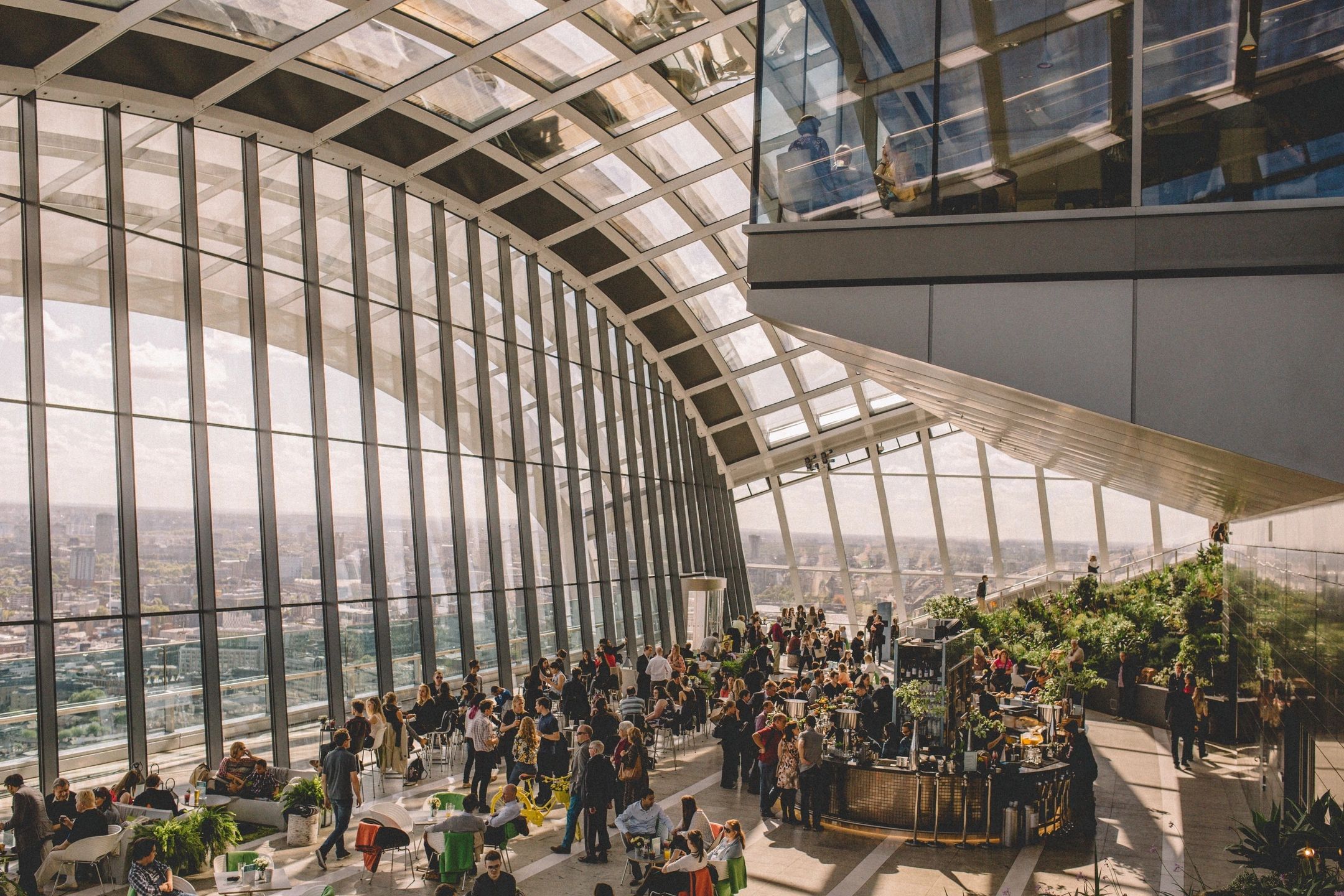 People in a large hotel atrium milling around a modern-looking bar at sunset