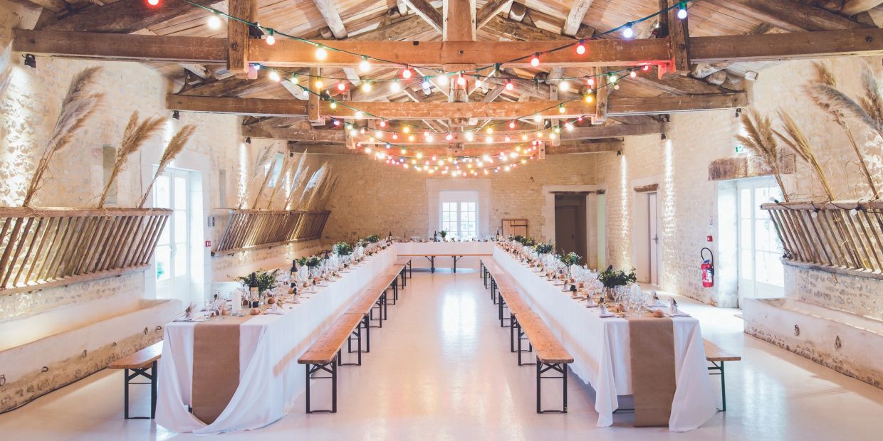 Rustic banquet hall with long tables and colorful string lights.