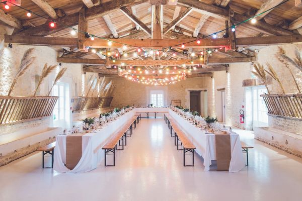 Rustic banquet hall with long tables and colorful string lights.