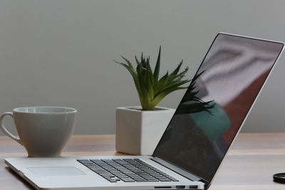 A sleek laptop on a wooden desk with a coffee cup and a small potted plant.