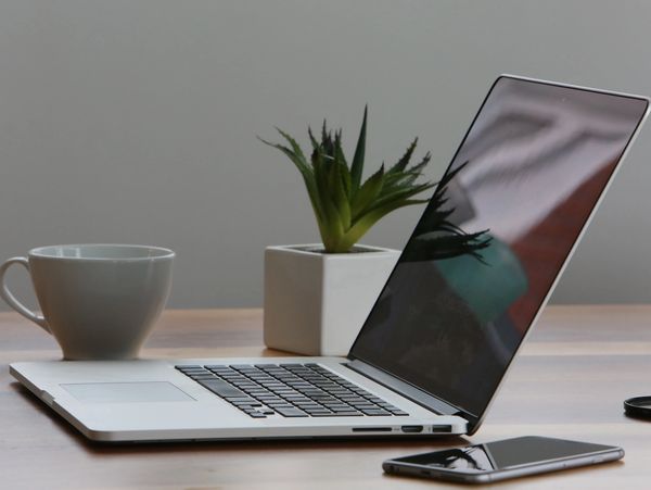 A desk with a laptop, a coffee mug, a phone and a plant