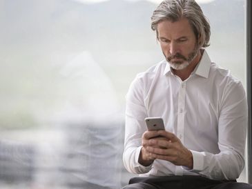 Middle-aged man in white shirt focused on his smartphone.