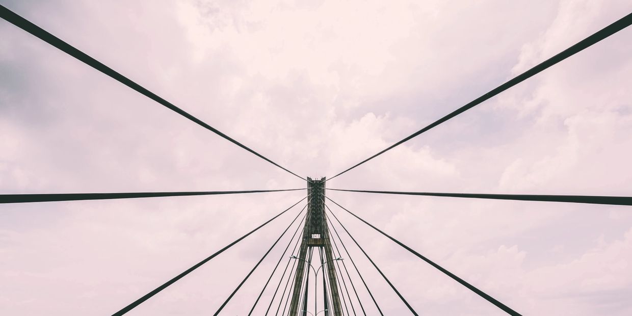 Symmetrical cables of a suspension bridge against a cloudy sky.