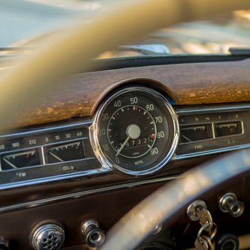 An image of an old car showing the dash and speedometer with key in ignition through steering wheel.