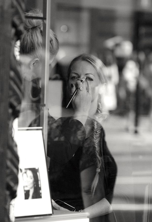 Make-up artist applying special occasion make-up on a client as seen through a window