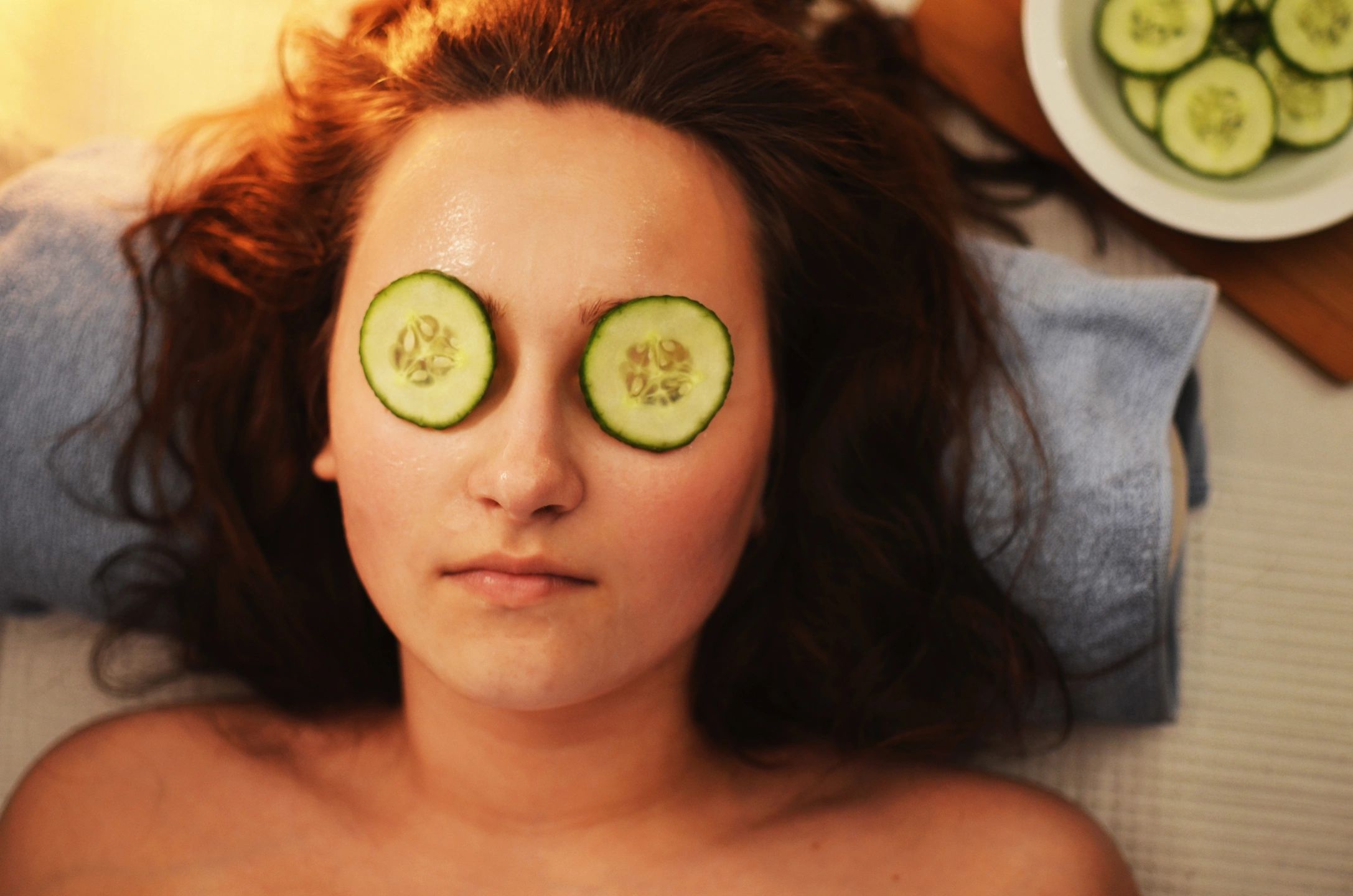 A woman is laying down with cucumber slices on her eyes.