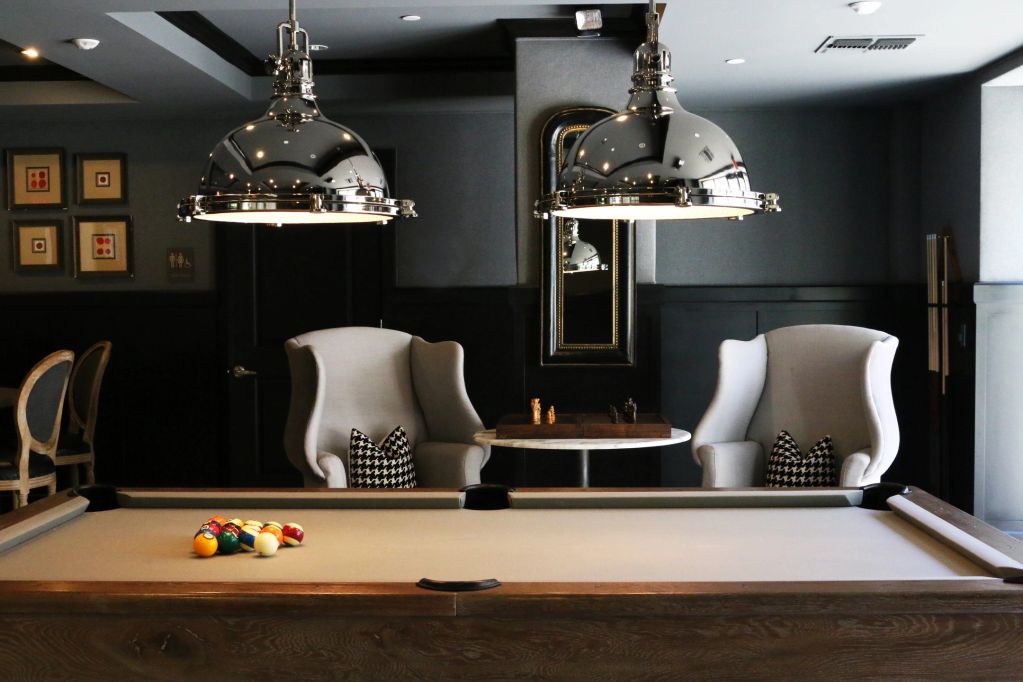 Elegant room with a pool table, two armchairs, and modern pendant lights.