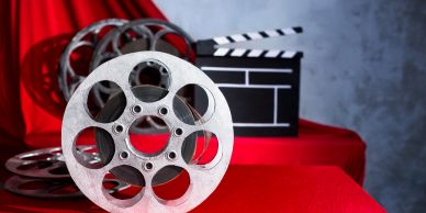 Film reels and a clapperboard on a red surface.