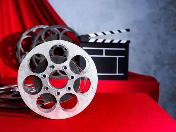 Old film reels and a clapperboard on a red cloth background.