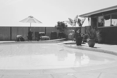 Empty outdoor swimming pool area with potted plants and an umbrella.