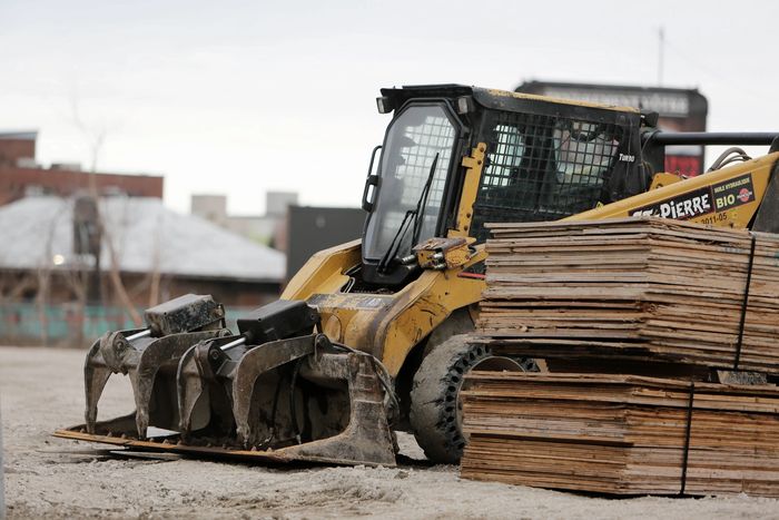 Construction loader with grapple attachment parked beside stacked wooden planks.