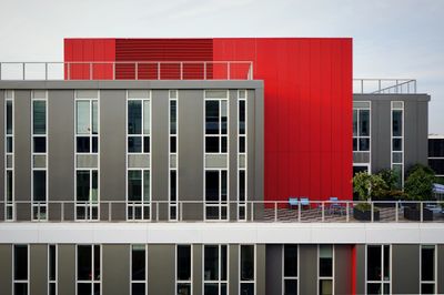 Modern building facade with gray and striking red panels and multiple windows.