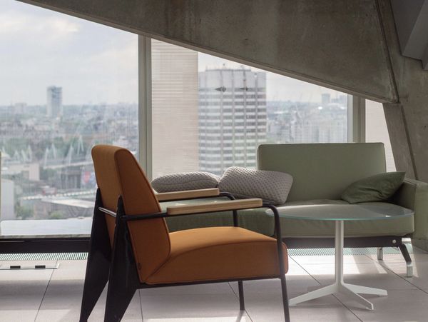Modern seating area with orange chair and green sofa by large window.