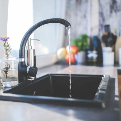 Modern kitchen sink with running water from black faucet.