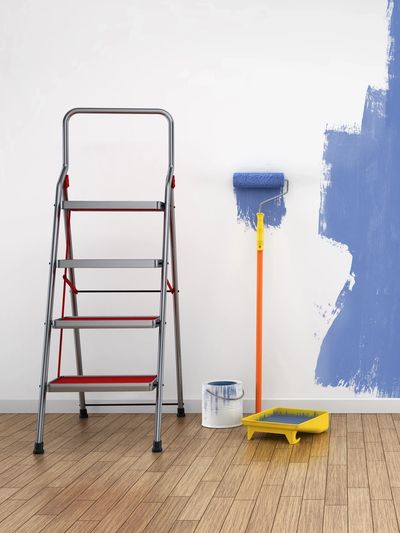 Step ladder and painting tools beside a partially painted blue wall.