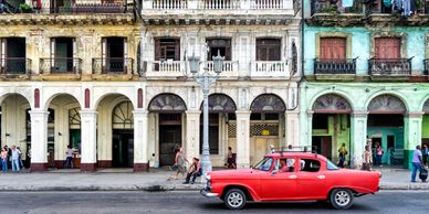 A red vintage car parked in front of colorful colonial buildings.
