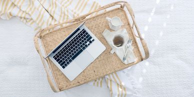 A cozy setup with a laptop and tea on a wicker tray over a white bedspread.