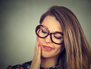 Woman with glasses touching her cheek in discomfort.