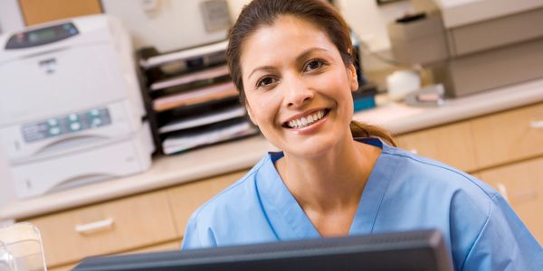 Smiling healthcare worker in blue scrubs at a desk.