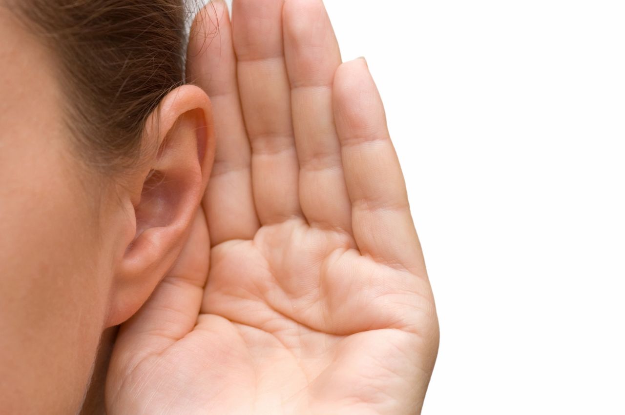 A person cusps their ear as the listen acutely.