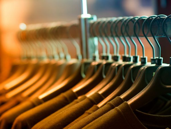 Row of brown shirts neatly hung on black hangers in warm lighting.