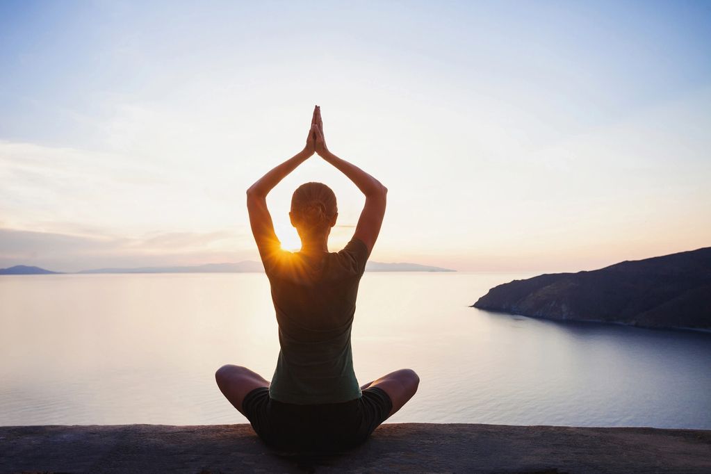Person practicing yoga at sunrise by the sea.