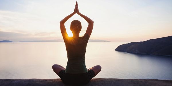 Person practicing yoga meditation at sunrise by the sea.