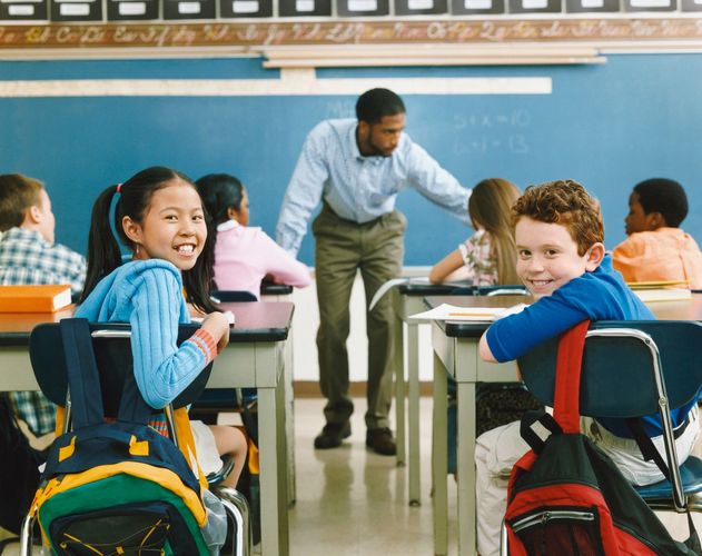 Two children one a girl and the other a boy sitting in class smiling. 