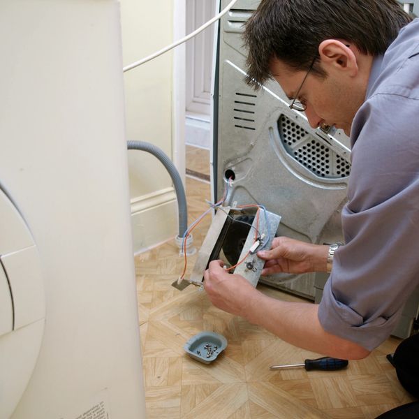 Man repairing a washing machine with tools on the floor.
