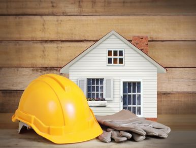 Yellow construction helmet and gloves with a model house in the background.