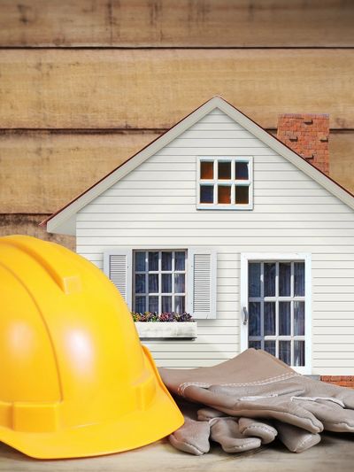 Model house with a hard hat and gloves, symbolizing home renovation.