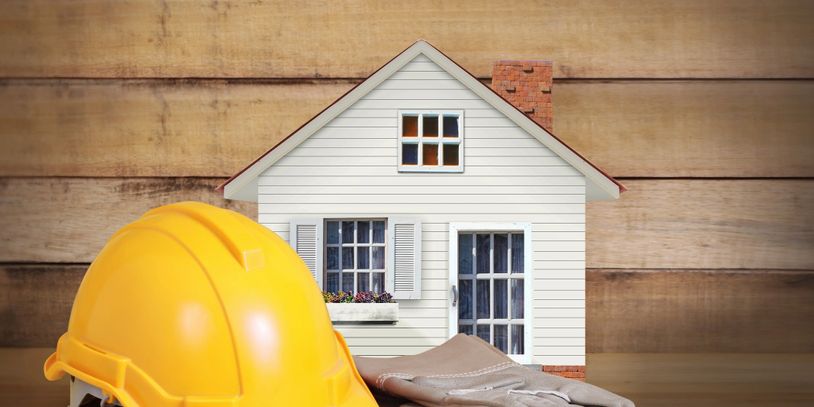 A yellow construction helmet and gloves in front of a model house.