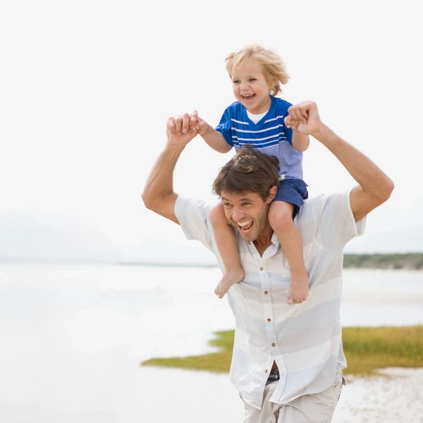 A joyful father carrying his laughing son on his shoulders by the beach.