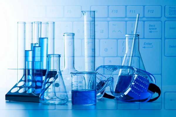 Laboratory glassware filled with blue liquid against a keyboard backdrop.