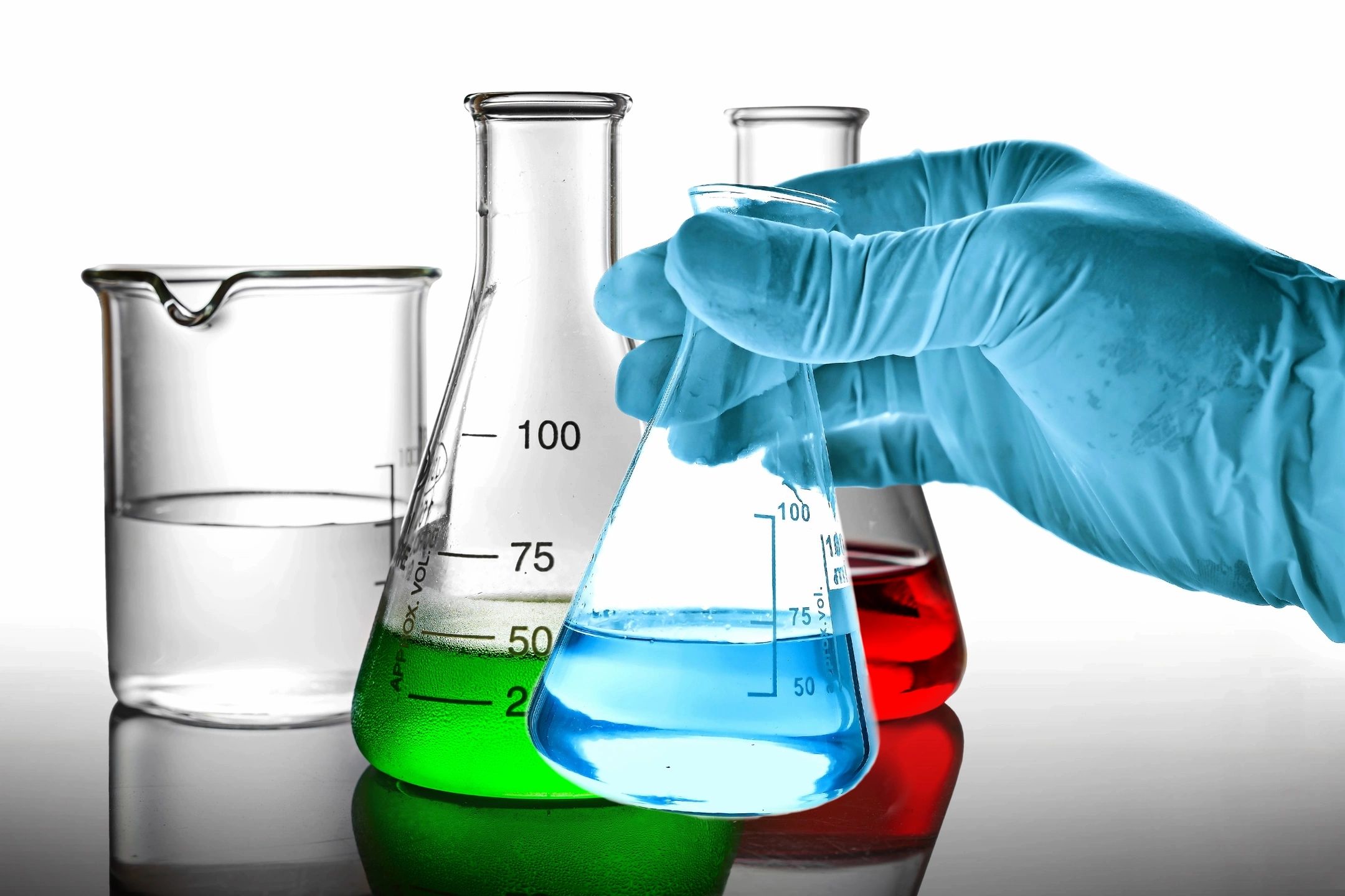 Gloved hand holding a flask with blue liquid among other colorful chemical beakers.