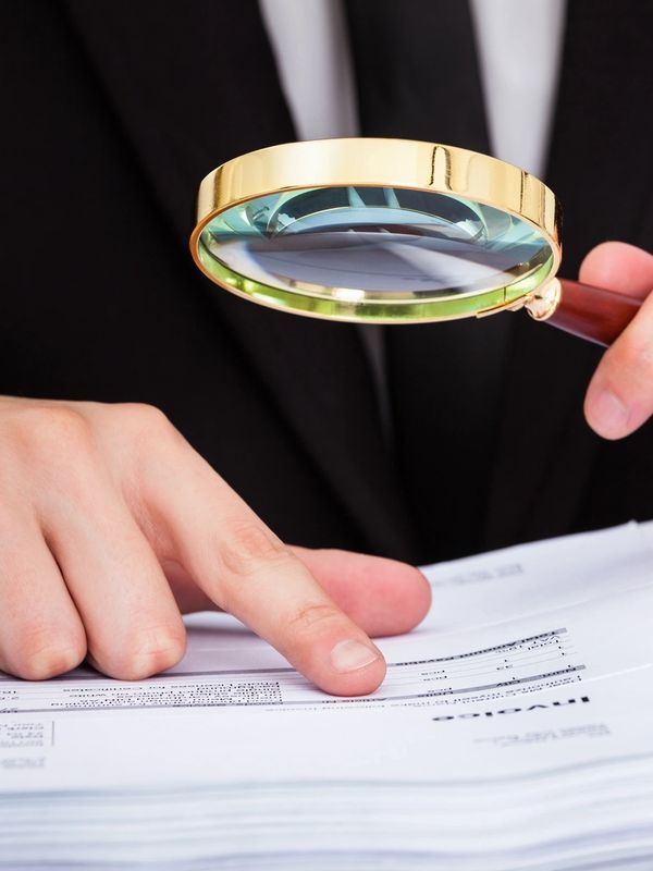 Person hold a loop in his hand and look in documents trough her.