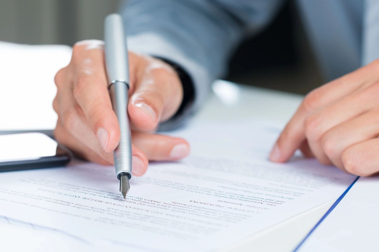 Person hold a fountain pen and reviews paperwork to make sure results and goals are aligned.