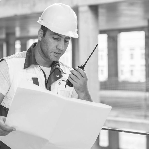 Construction worker in helmet using walkie-talkie and reading plans.