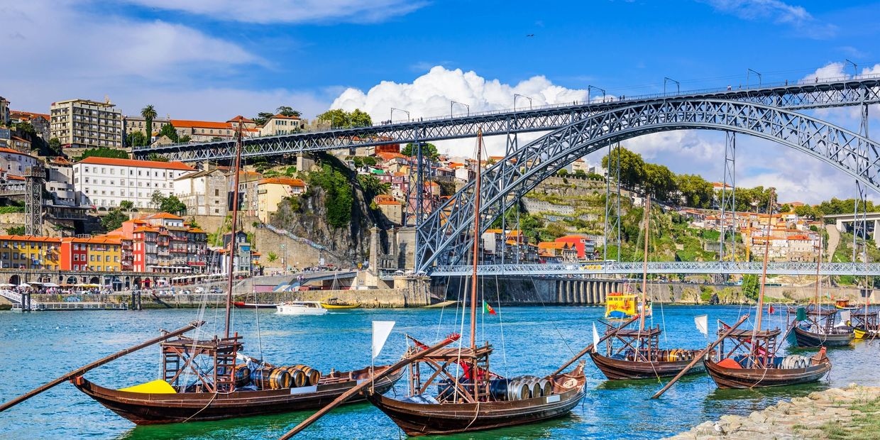 Traditional boats on a river with a large iron bridge and colorful buildings in the background.