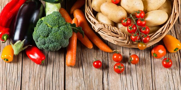 Fresh vegetables including carrots, potatoes, broccoli, and tomatoes on a wooden surface.