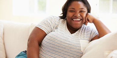 Smiling woman relaxing on a white couch in a bright room.