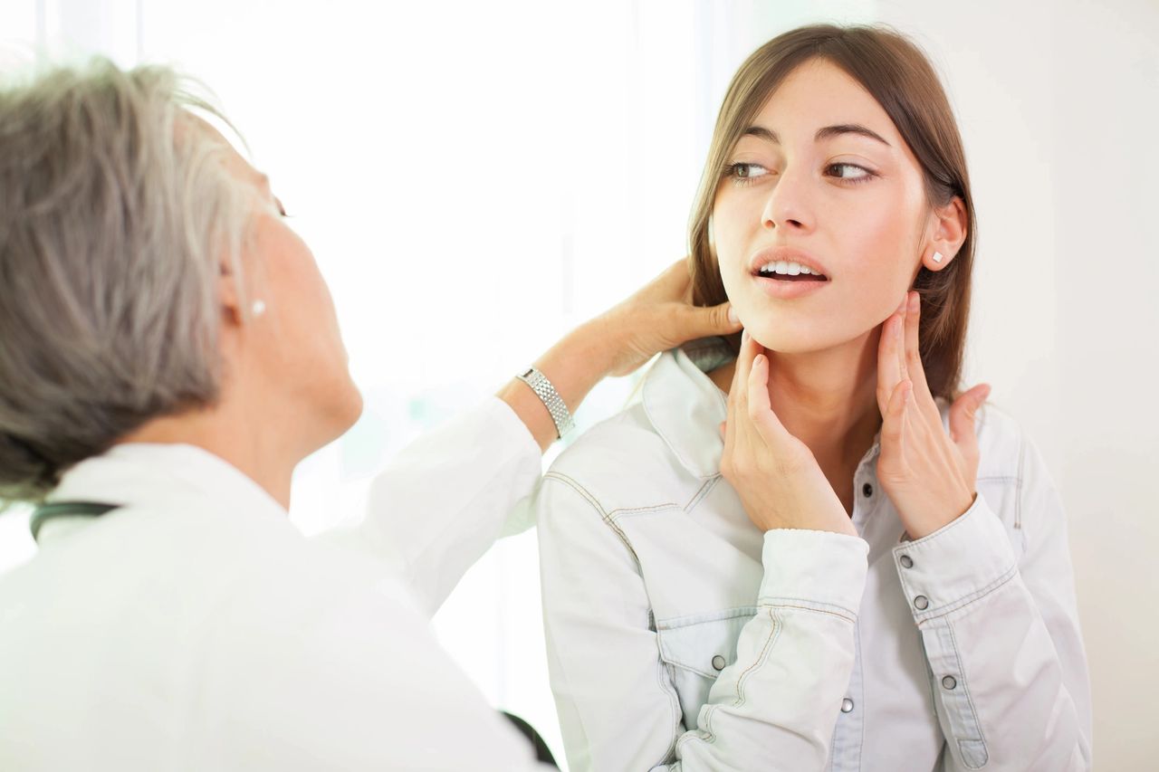 A doctor examining a young woman's neck and throat.