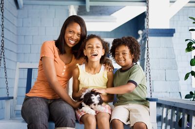 Smiling woman and two children sitting on a porch swing with a puppy.