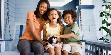 A happy family sitting on a porch swing with a small puppy.