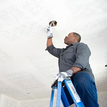 Man on ladder inspecting ceiling hole.