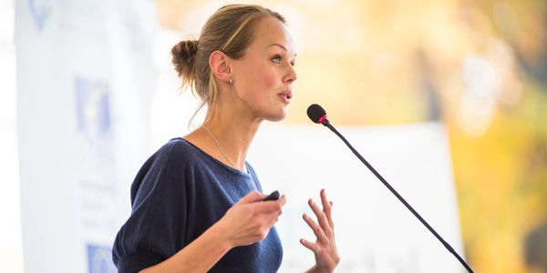 Woman standing at a lectern speaking to an unseen audience. 