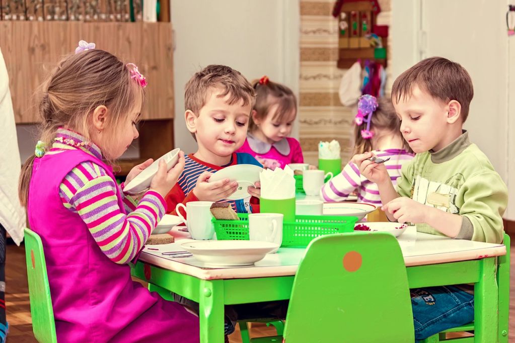 Children eating together at a table in a colorful room.