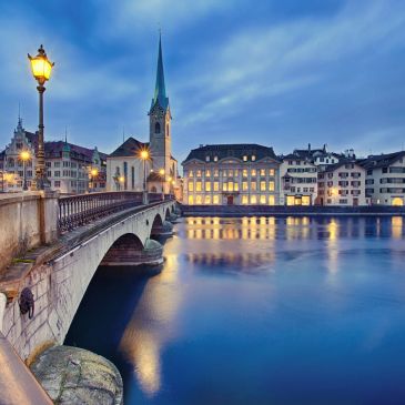 Evening view of a historic bridge and illuminated buildings by a calm river.