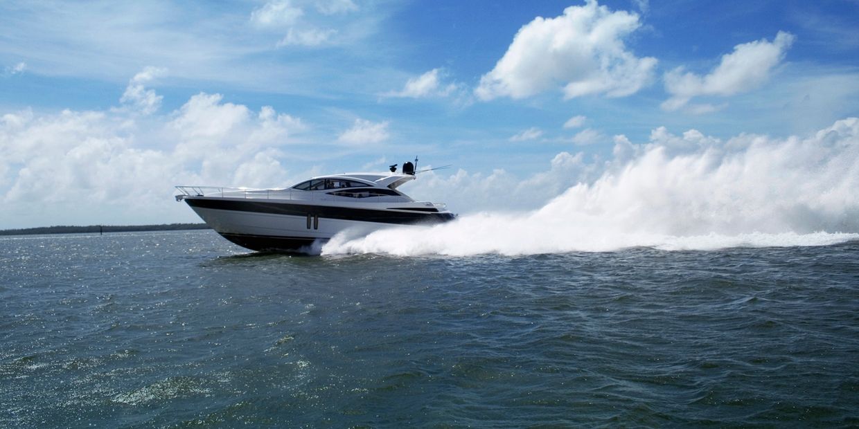 A sleek yacht speeds across the water under a bright blue sky.