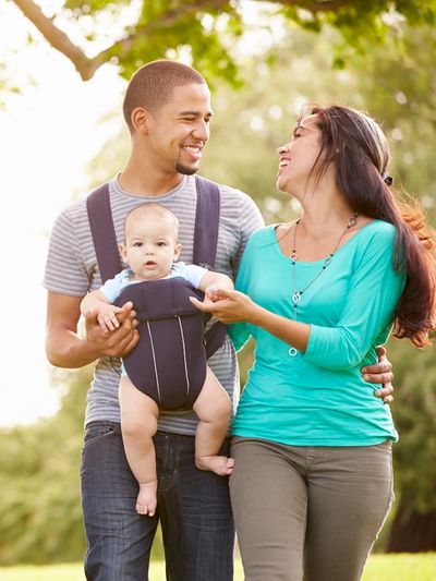 Happy family enjoying a walk outdoors with their baby in a carrier.